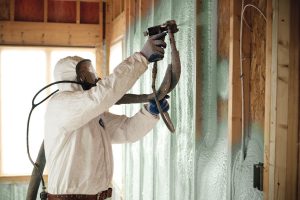 Worker in protective gear applies spray foam insulation to unfinished walls