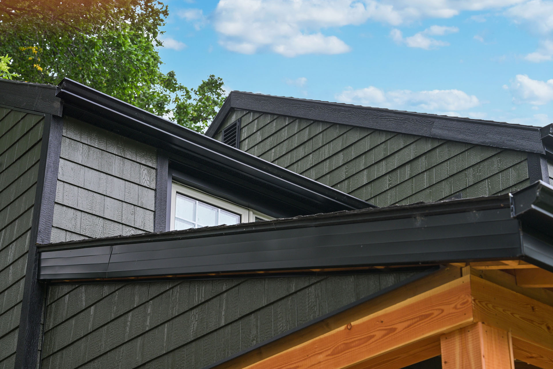 Close-up of green siding home with black shingle roof and white window.